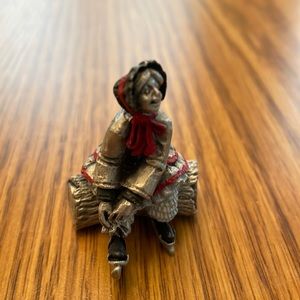 Pewter lady sitting on log, tying her ice skates.